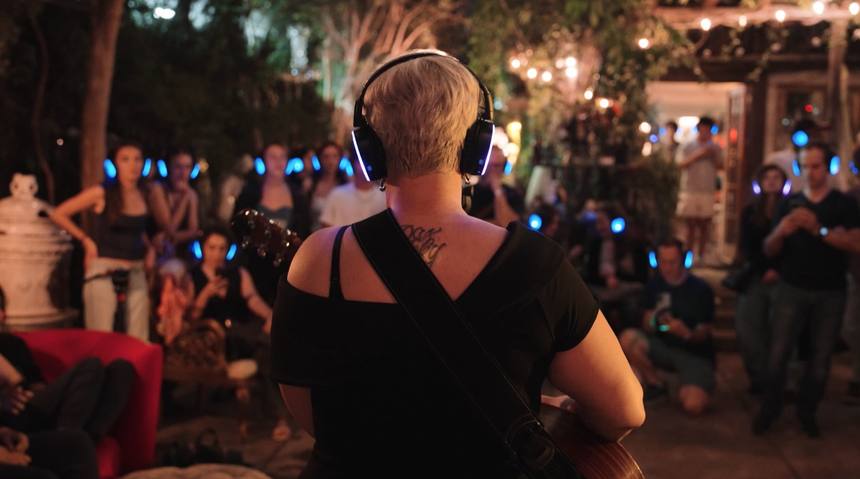 Guitarist facing a garden crowd wearing glowing blue headphones